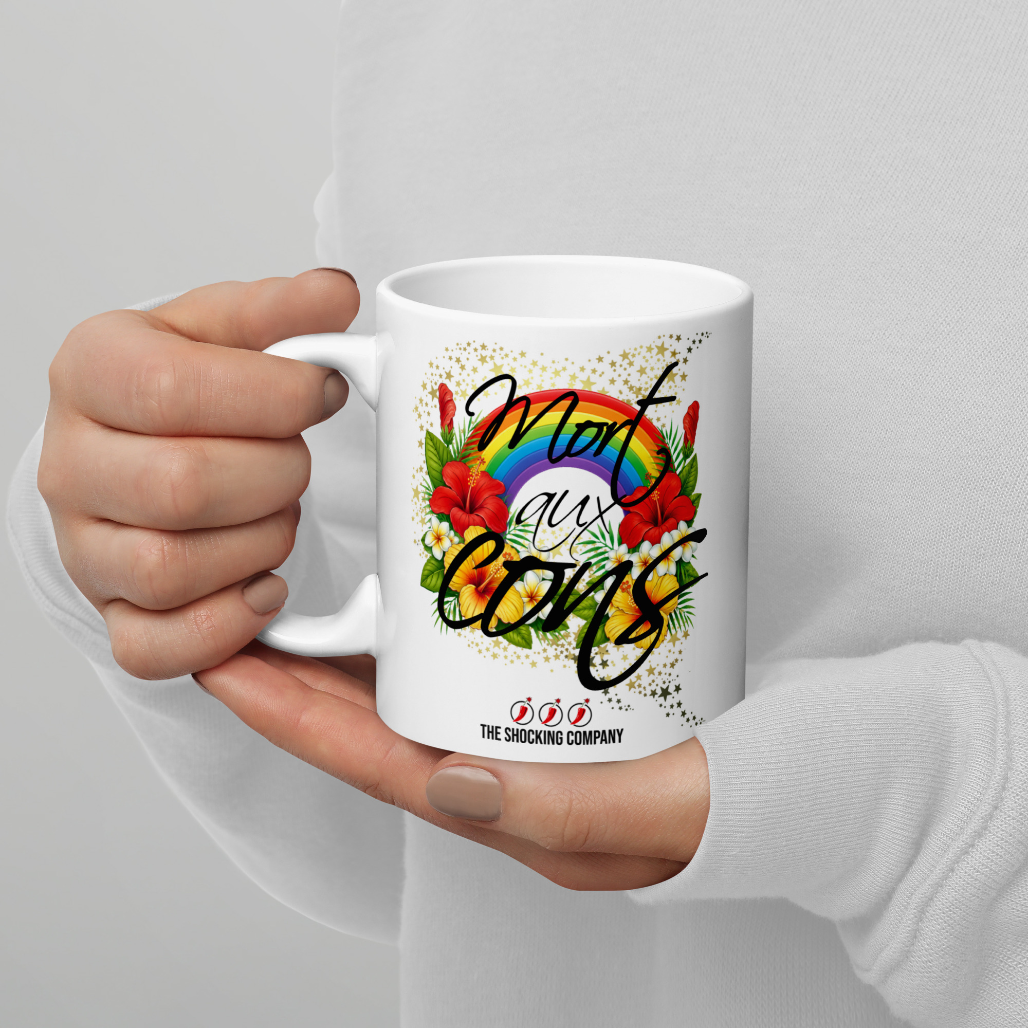 Tasse avec l’inscription “Mort aux cons” entourée de fleurs tropicales colorées, d’un arc-en-ciel et d’étoiles.